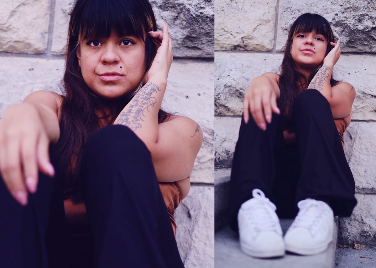 Portret kobiety z tatuażem na ramieniu, siedzącej na tle kamiennej ściany, ujęcie z dołu.