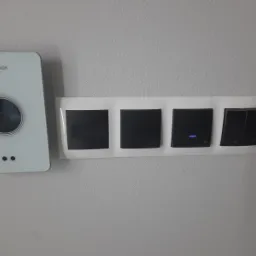 Biały panel sterowania Bosch z dotykowym ekranem oraz cztery czarne włączniki światła z białymi ramkami zamontowane na szarej ścianie.