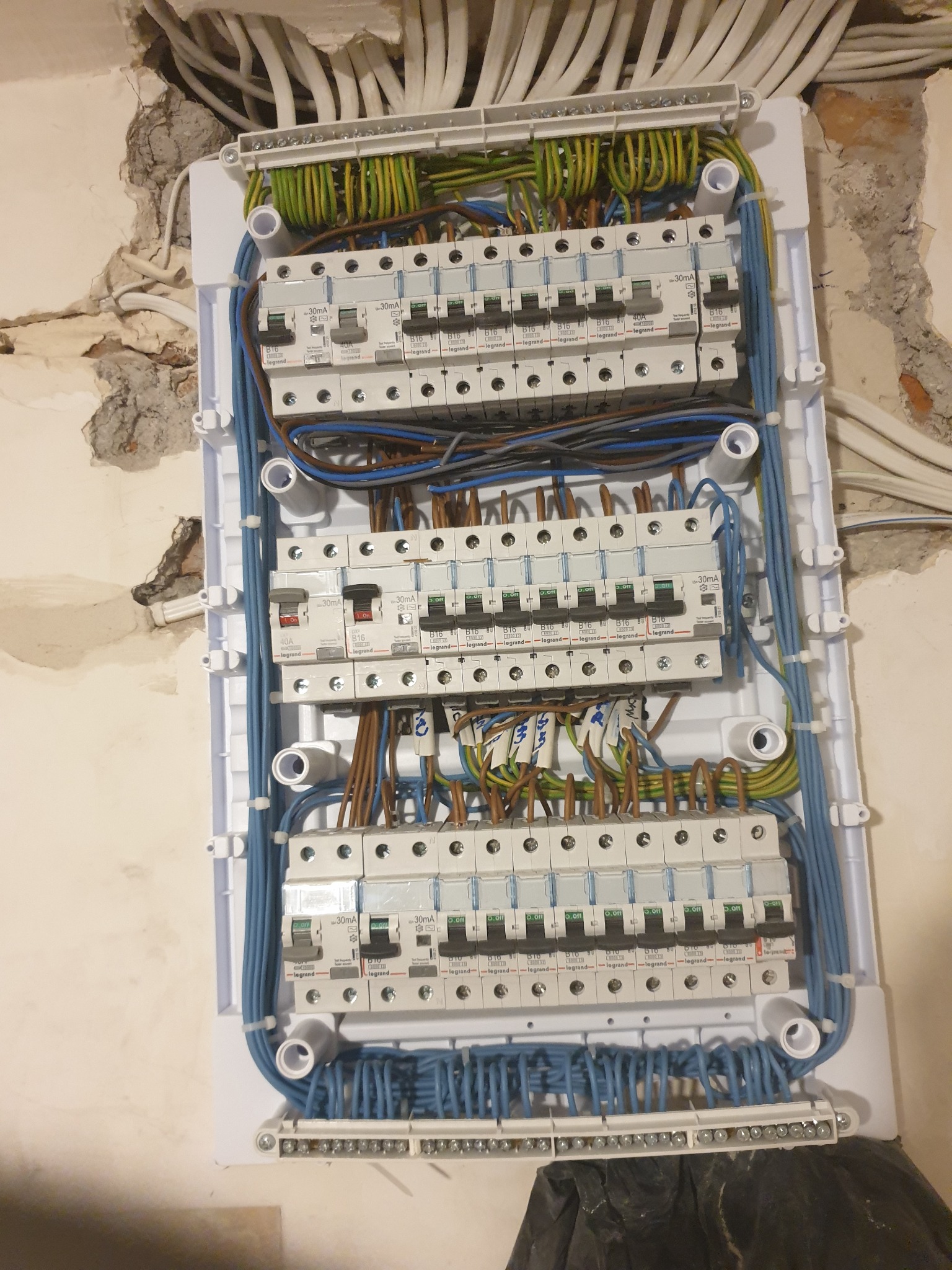 Rozdzielnica elektryczna z zainstalowanymi bezpiecznikami Legrand, widoczne przewody w różnych kolorach, tło stanowią ściany w trakcie remontu.