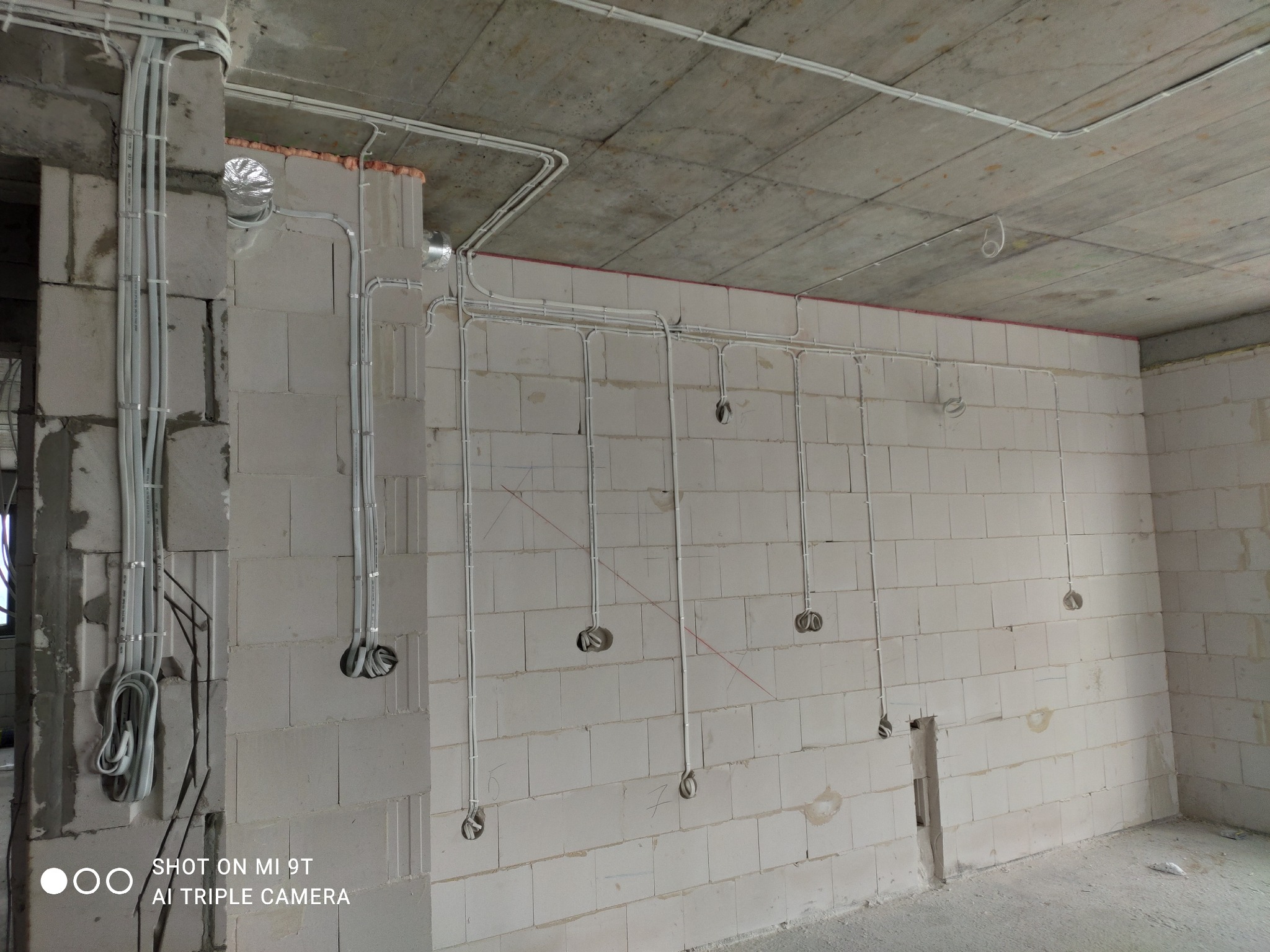 Surowe wnętrze z widocznymi przewodami elektrycznymi prowadzonymi po ścianach z bloczków i pod sufitem, przygotowane pod gniazdka i oświetlenie.