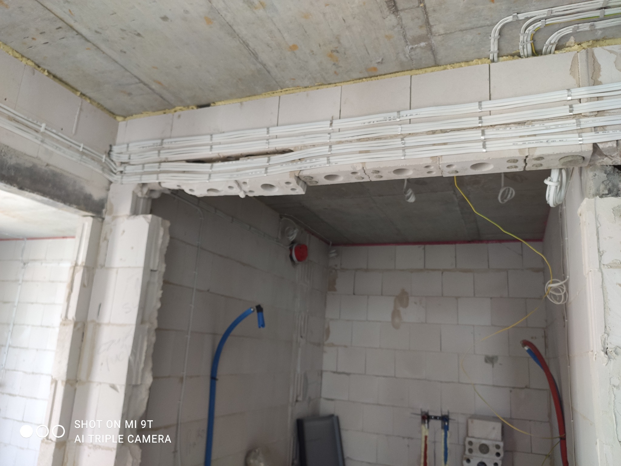 Wewnętrzne okablowanie w nowym budynku z białych bloków, kable przymocowane do sufitu i ścian za pomocą metalowych uchwytów, żółte przewody zwisające z sufitu