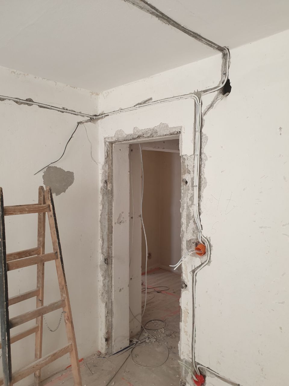 Wnętrze w trakcie remontu w Warszawie z widocznymi przewodami elektrycznymi prowadzonymi po ścianach i suficie, pomarańczowe puszki instalacyjne oraz drewniana drabina oparta o ścianę.
