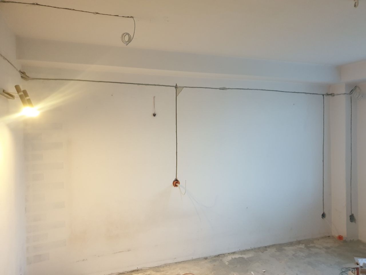 Wnętrze w trakcie prac elektrycznych: przewody prowadzone po ścianach i suficie, puszki instalacyjne zamontowane, widoczne prowizoryczne oświetlenie.