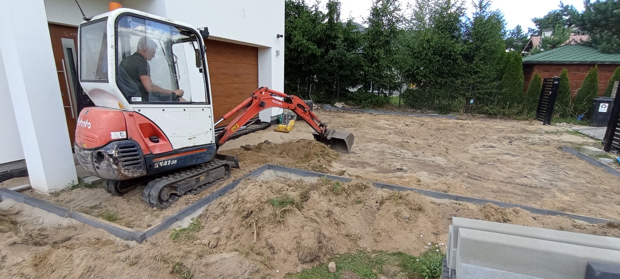 Mini koparka Kubota przygotowuje teren pod przyszłą nawierzchnię, widoczne obrzeża i piasek.
