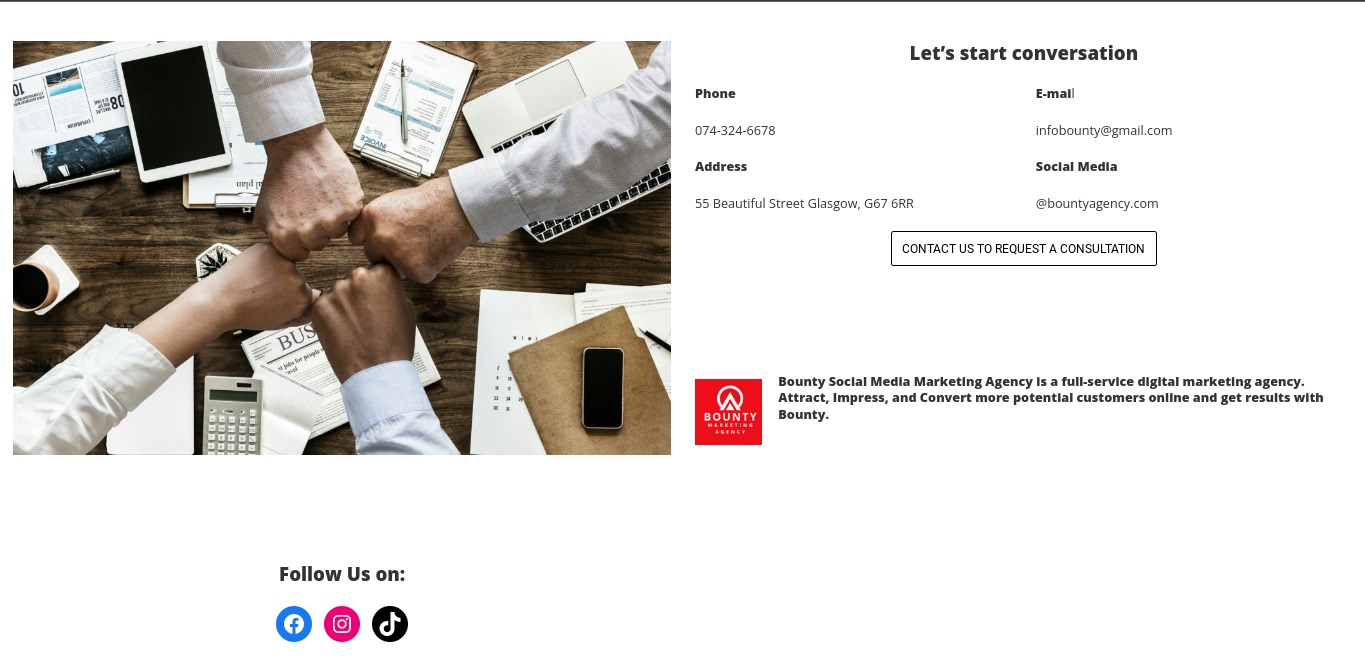 Zespół zjednoczony w geście solidarności, z dłońmi złączonymi nad drewnianym biurkiem, na którym leżą tablet, laptop, dokumenty, kalendarz, telefon i kalkulator.