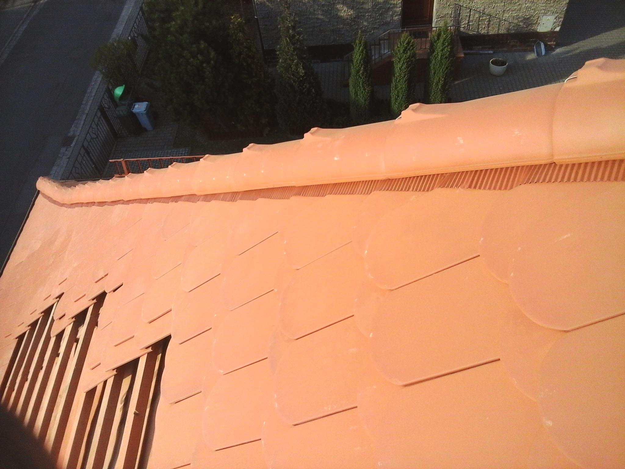 Nowy, pomarańczowy dach z okrągłych dachówek z widokiem na rynnę i otoczenie budynku z perspektywy z góry.