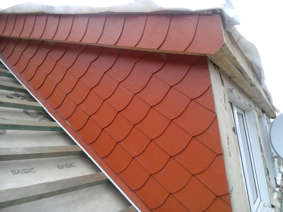 Fragment dachu z nowym, czerwonym pokryciem przypominającym łuskę, widoczne elementy konstrukcji dachu i okno.