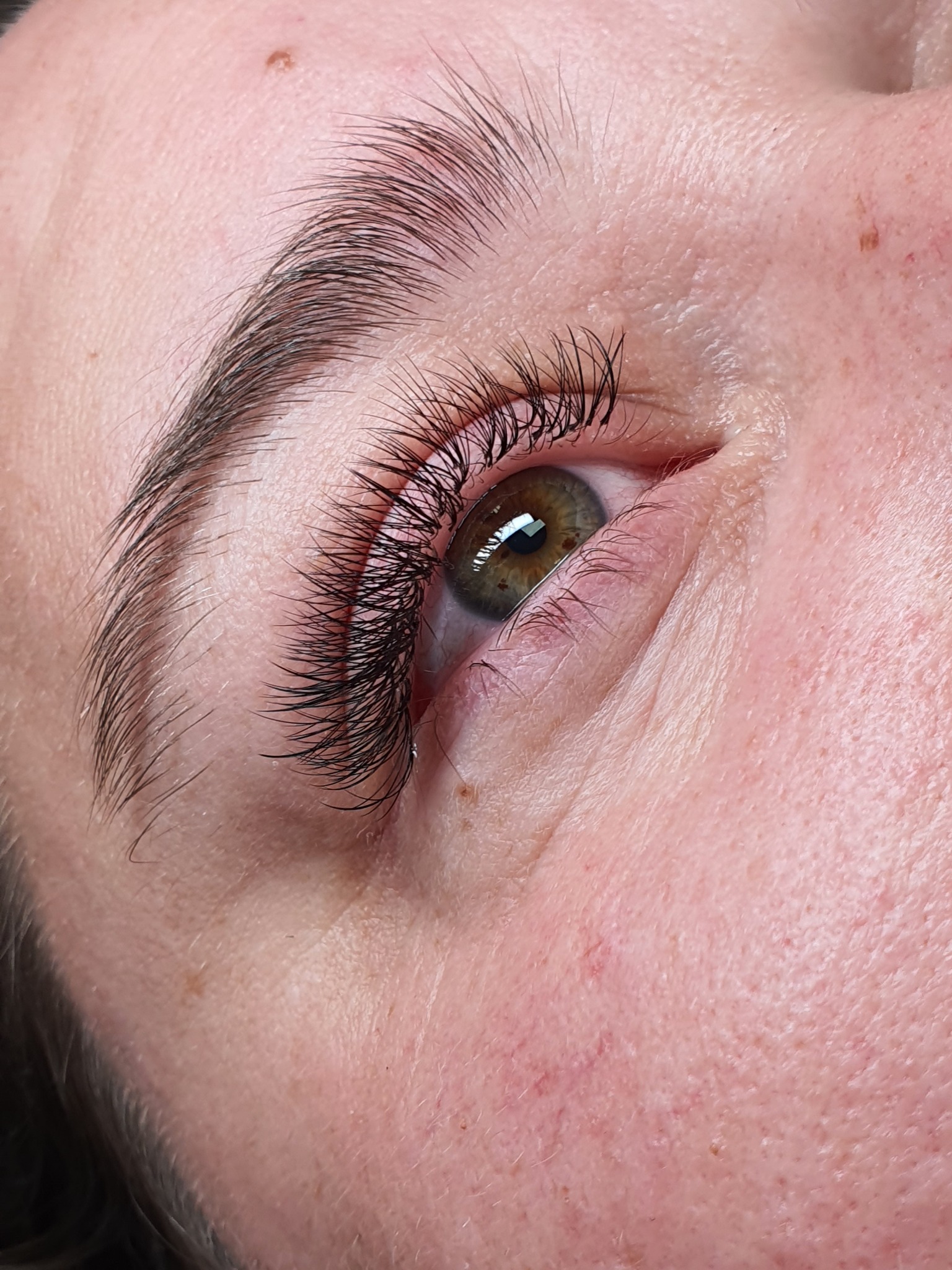 Zbliżenie na oko z wyraźnie przedłużonymi, gęstymi rzęsami; widoczne drobne naczynka na skórze wokół oka oraz naturalny kształt brwi.
