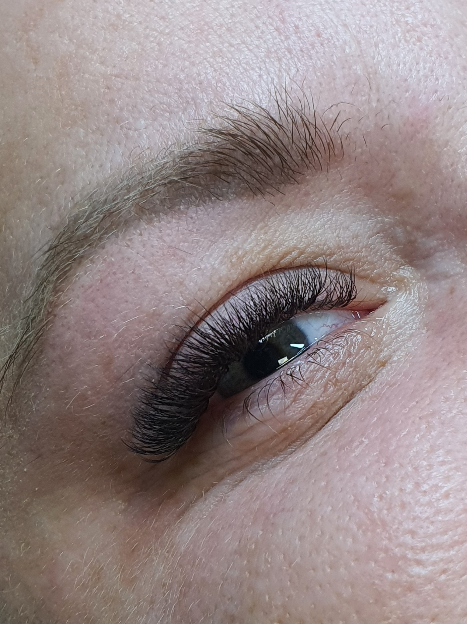 Zbliżenie na oko z przedłużonymi, gęstymi rzęsami w odcieniu czerni. Widoczna delikatna skóra wokół oka i naturalny kształt brwi.