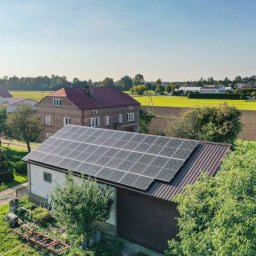 MR Energy Spółka z Ograniczoną Odpowiedzialnością - Instalacja paneli słonecznych na dachu budynku gospodarczego z białej cegły, widok z góry na wiejski krajobraz w tle.