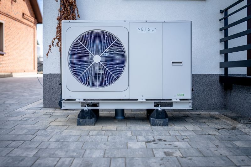 Zewnętrzna jednostka pompy ciepła Netsu, zamontowana na metalowej ramie z czarnymi podkładkami antywibracyjnymi, na tle białej ściany budynku z elementami dekoracyjnymi.
