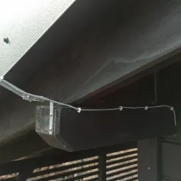 Czujnik deszczu modelu RSD8BEX zamontowany pod zadaszeniem, z widocznymi przewodami przymocowanymi klipsami do drewnianej belki.