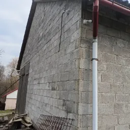 Zewnętrzny mur budynku z betonu komórkowego z zamontowanymi dwiema kamerami monitoringu, rurą spustową i kablem antenowym, widok z dołu.