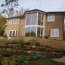 Ar-Wi - Dom z cegły z nową, przeszkloną dobudówką, widok z ogrodu z tarasami i roślinnością.