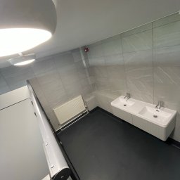 Ar-Wi - Nowoczesna łazienka z dwoma umywalkami nablatowymi i grzejnikiem panelowym, wykończona płytkami imitującymi marmur, oświetlona lampą sufitową.