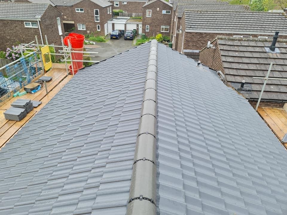 Szary dach z dachówki ceramicznej po renowacji, widok z góry, rusztowanie z boku, w tle zabudowa jednorodzinna.