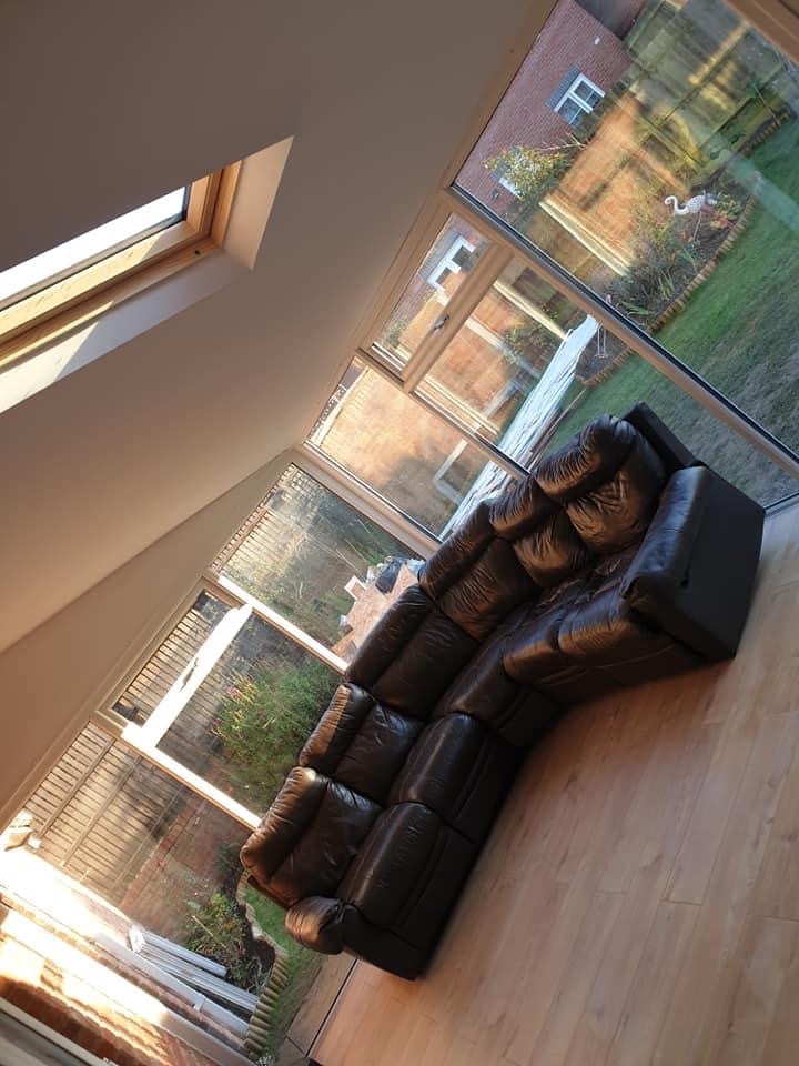 Jasne wnętrze z dużym narożnikiem ze skóry w odcieniach brązu, widok na ogród przez panoramiczne okna i okno dachowe, parkiet na podłodze.