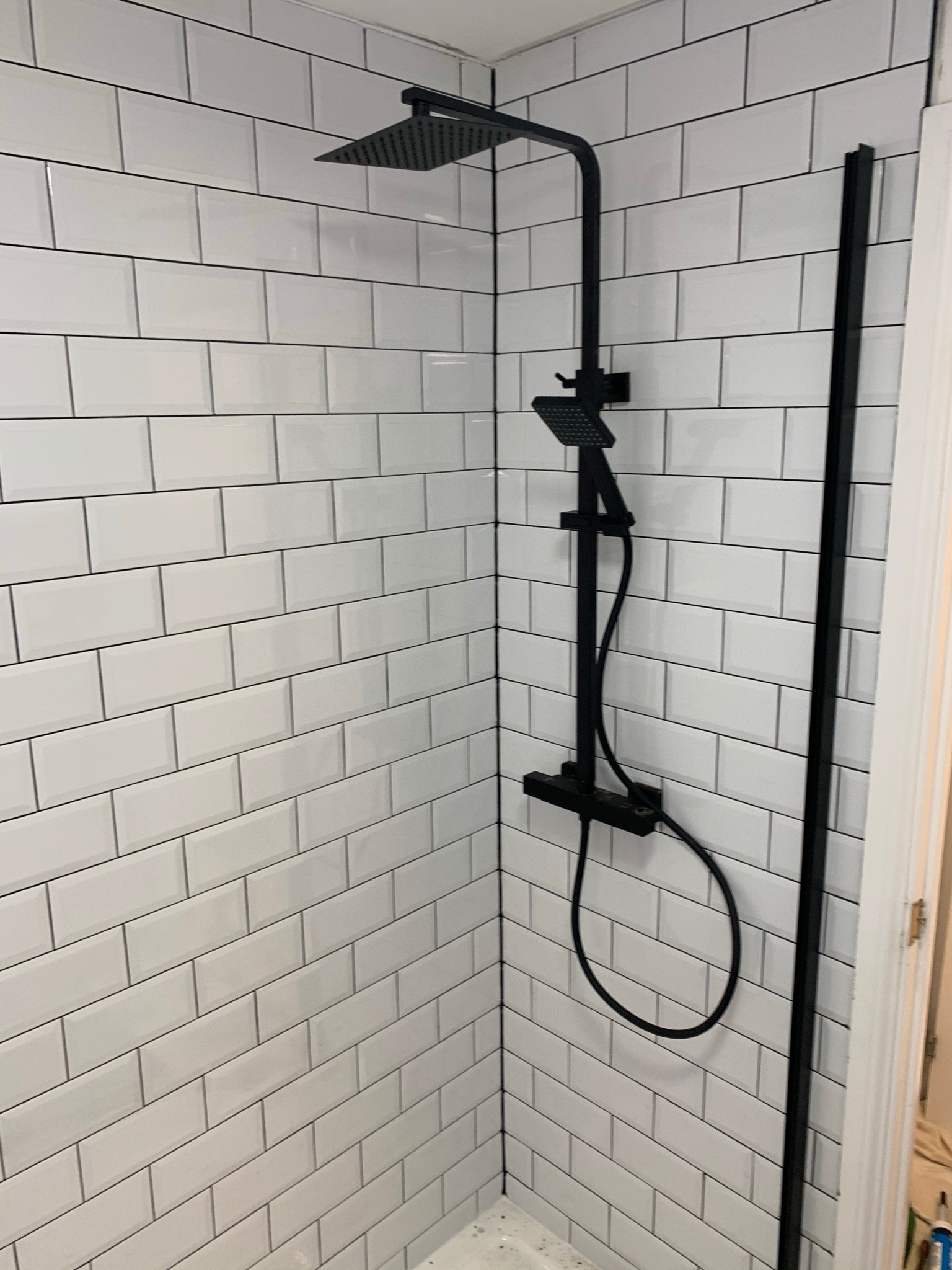 Nowoczesna kabina prysznicowa z czarną armaturą i białymi, prostokątnymi płytkami ułożonymi w cegiełkę.