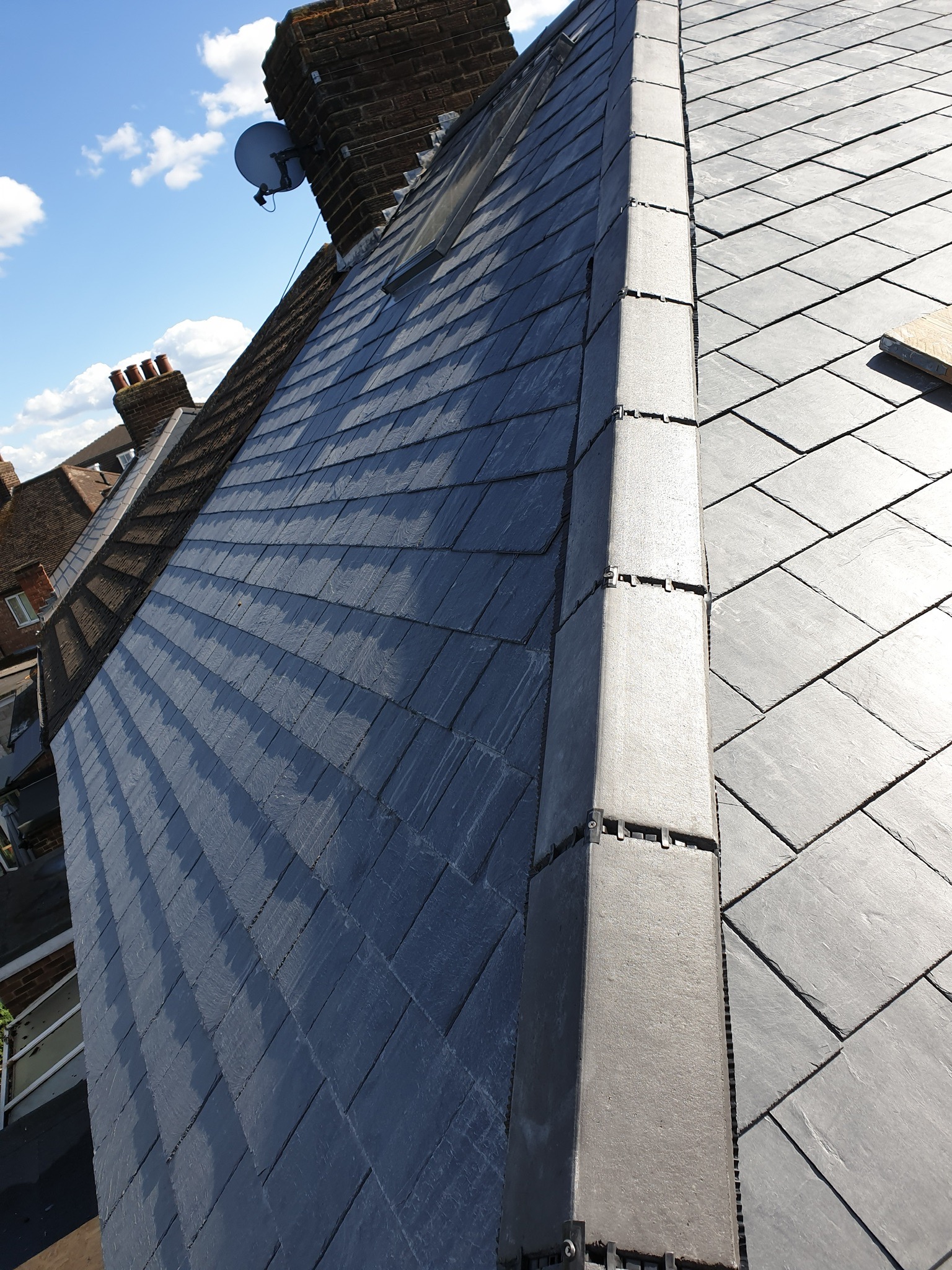 Nowy dach z szarej łupkowej dachówki ułożony na budynku mieszkalnym, widok z góry, z widocznymi kominami i anteną satelitarną w tle.