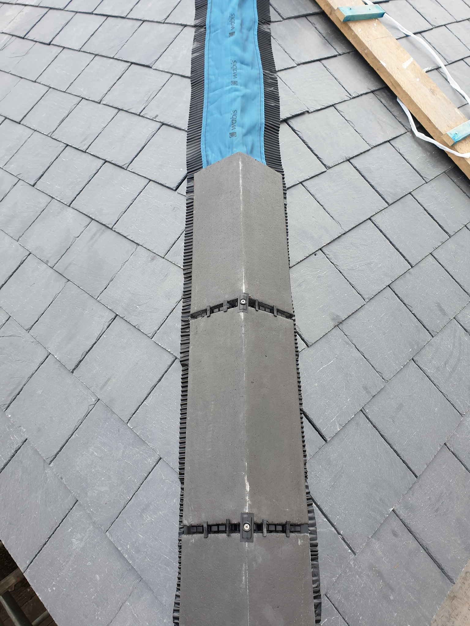 Szczegółowe ujęcie fragmentu dachu pokrytego łupkiem z widocznym systemem wentylacji kalenicy i elementami mocującymi, ukazujące detale konstrukcyjne.