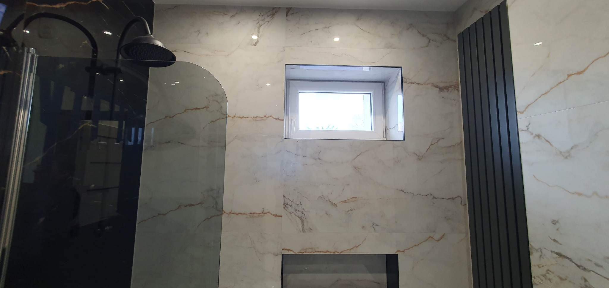 Wykończona łazienka z marmurowymi płytkami, czarną kabiną prysznicową typu walk-in z deszczownicą, grzejnikiem panelowym i oknem w ścianie.