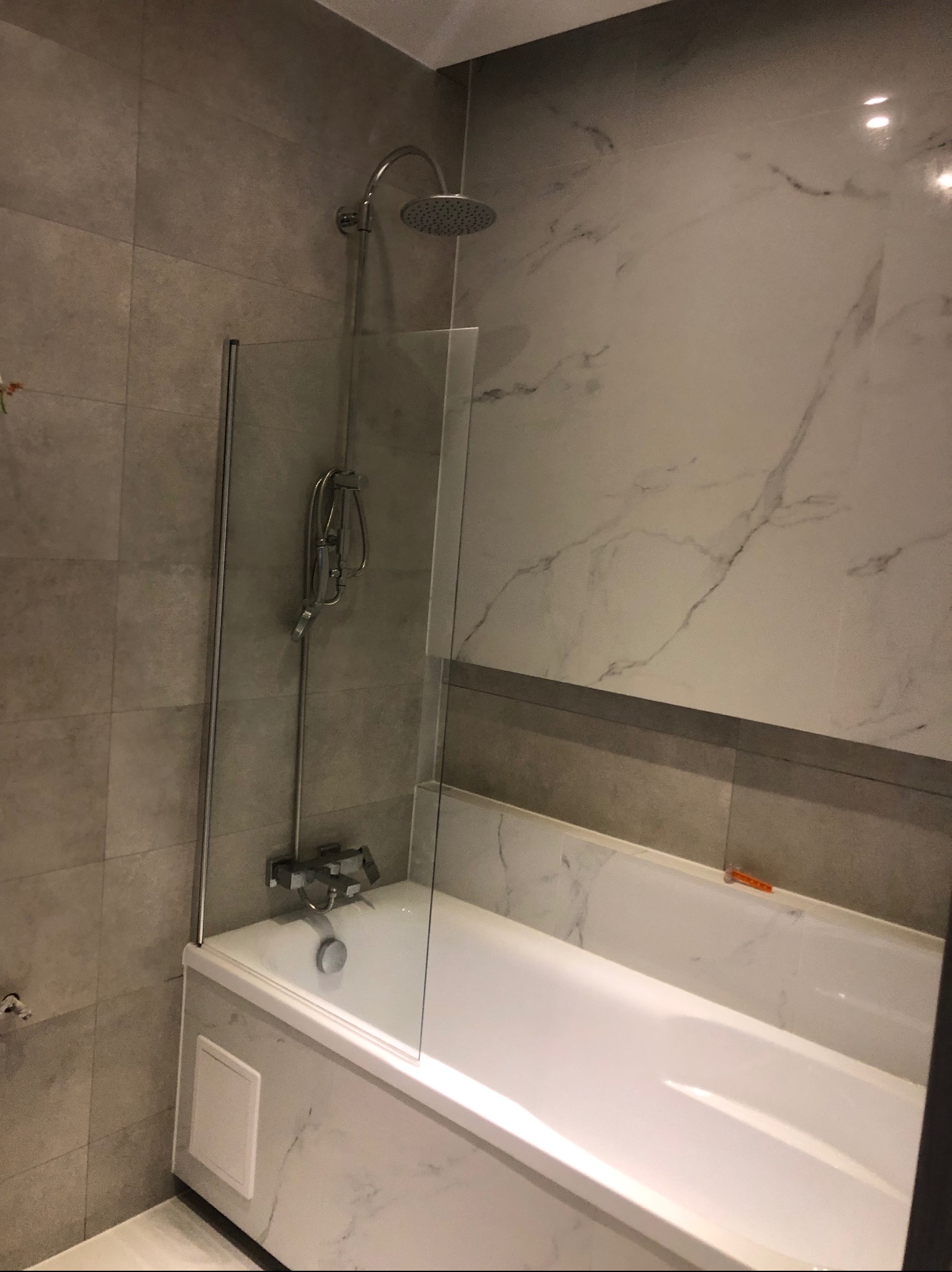 Nowoczesna łazienka z wanną obudowaną marmurowymi płytami, przeszklonym parawanem nawannowym i chromowaną armaturą prysznicową.