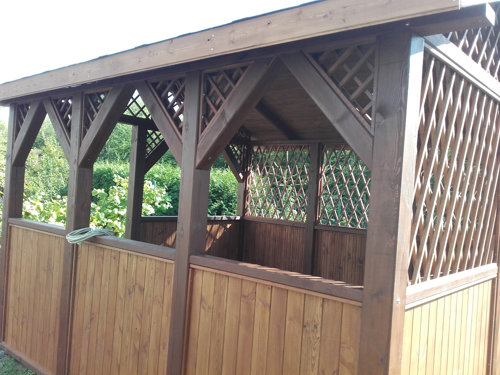 Drewniana konstrukcja z ażurowymi ścianami, widoczne elementy z ciemnego i jasnego drewna, na dolnej krawędzi leży zwój sznura.