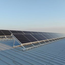 WILUX - Rząd paneli fotowoltaicznych bifacial na konstrukcji wsporczej, zamontowanych na blaszanym dachu budynku przemysłowego w słoneczny dzień.