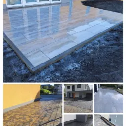 Ułożona, mokra, prostokątna kostka brukowa imitująca drewno na tarasie przy domu z żółtą elewacją, widoczne ślady ziemi i przygotowania do dalszych prac wykończeniowych.