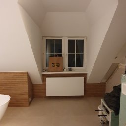 Smyd-bud - Poddasze po remoncie: beżowe płytki podłogowe, białe ściany, okno z torbą IKEA, grzejnik i drewniana boazeria do połowy ściany.