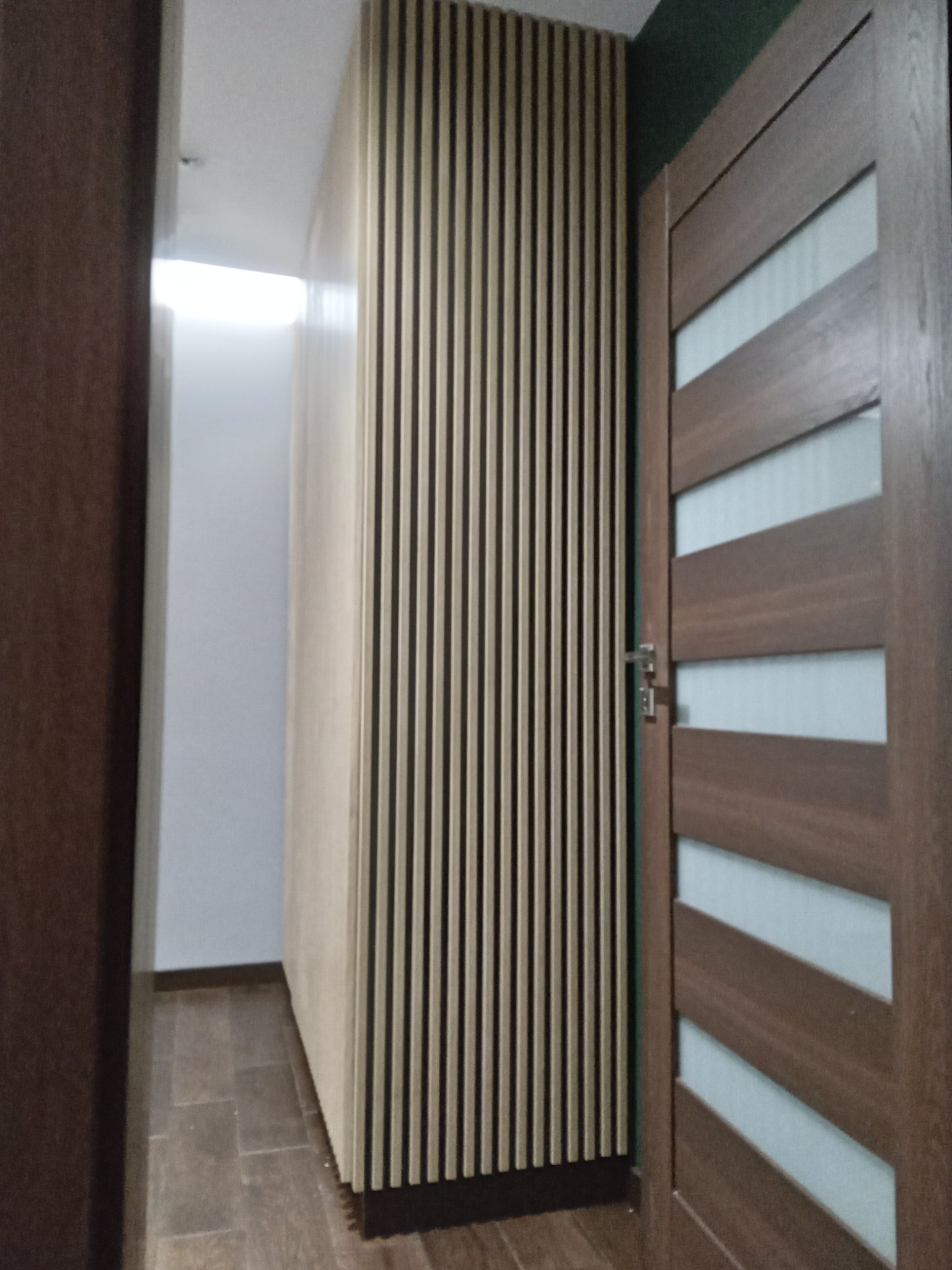 Nowoczesna szafa z lamelami w korytarzu, obok drewniane drzwi z poziomymi przeszkleniami.