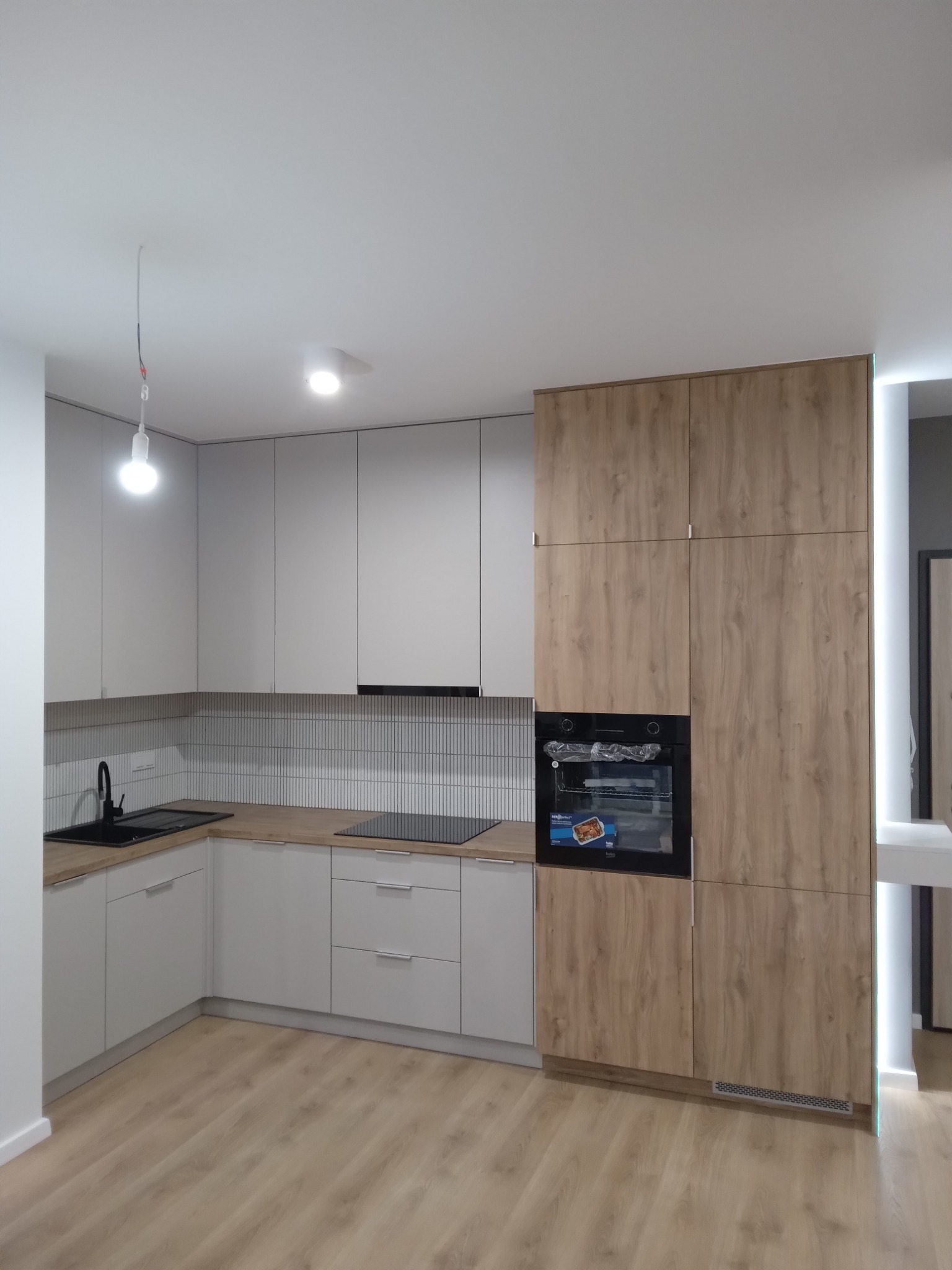 Nowoczesna kuchnia w odcieniach szarości i drewna z czarną armaturą, wykończona płytkami imitującymi cegłę, z piekarnikiem marki Beko.