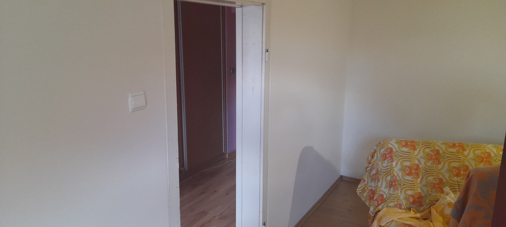 Jasny pokój po odświeżeniu: kremowe ściany, białe futryny drzwi, widoczny włącznik światła, częściowo zasłonięty fotel z wzorem w kwiaty.