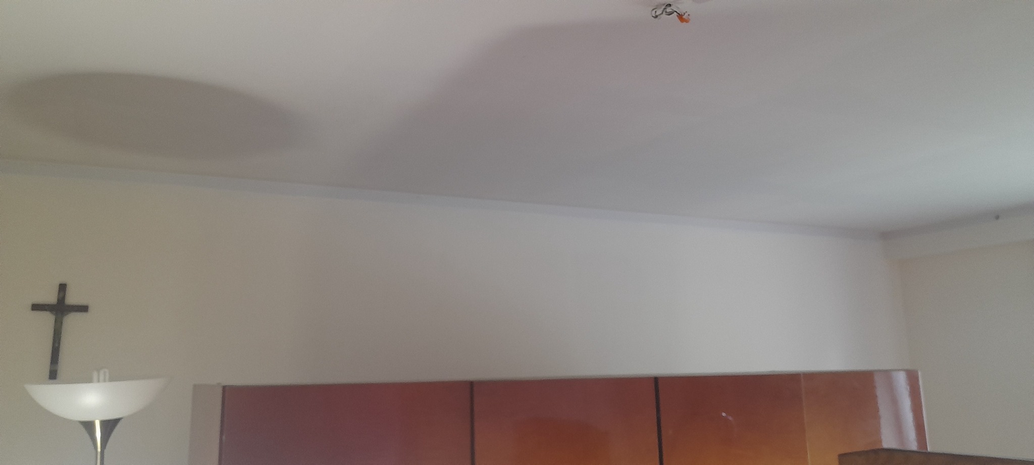 Biały sufit po malowaniu z widocznym cieniem lampy i elementami instalacji elektrycznej, fragment ściany z krzyżem i lampą stojącą.