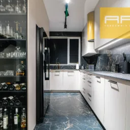 Nowoczesna kuchnia z białymi szafkami, czarnym blatem i marmurowym backsplashiem, uzupełniona o przeszkloną szafę na wino i alkohole po lewej stronie, oraz żółty okap.