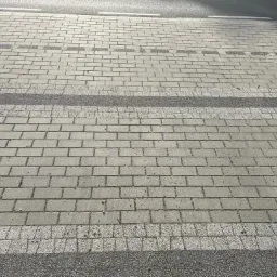 Szary chodnik z kostki brukowej w formie przejścia dla pieszych z paskami z drobnej kostki granitowej, widok z g&oacute;ry.