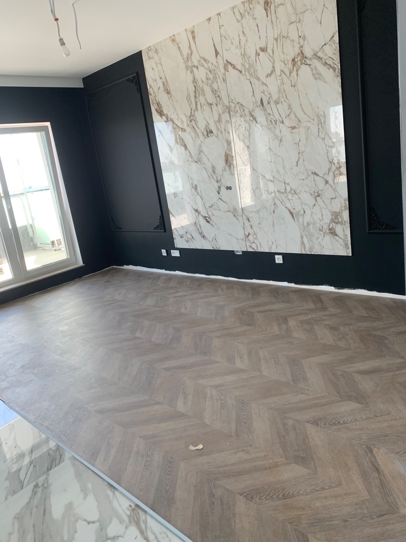 Pokój z parkietem ułożonym w jodełkę, ściany pomalowane na czarno z dekoracyjnymi sztukateriami, marmurowa płyta na ścianie, duże okno.