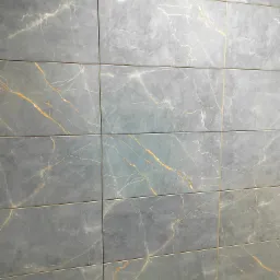 Szara ściana wyłożona prostokątnymi płytkami imitującymi marmur z delikatnymi złotymi żyłkami. Widoczne fugi podkreślają regularny układ.