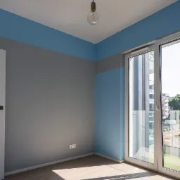 Wnętrze pokoju po malowaniu z poziomym podziałem kolorów: szary dół, niebieski górny pas. Widoczne drewniane panele podłogowe i nowoczesna lampa z dwiema żarówkami.