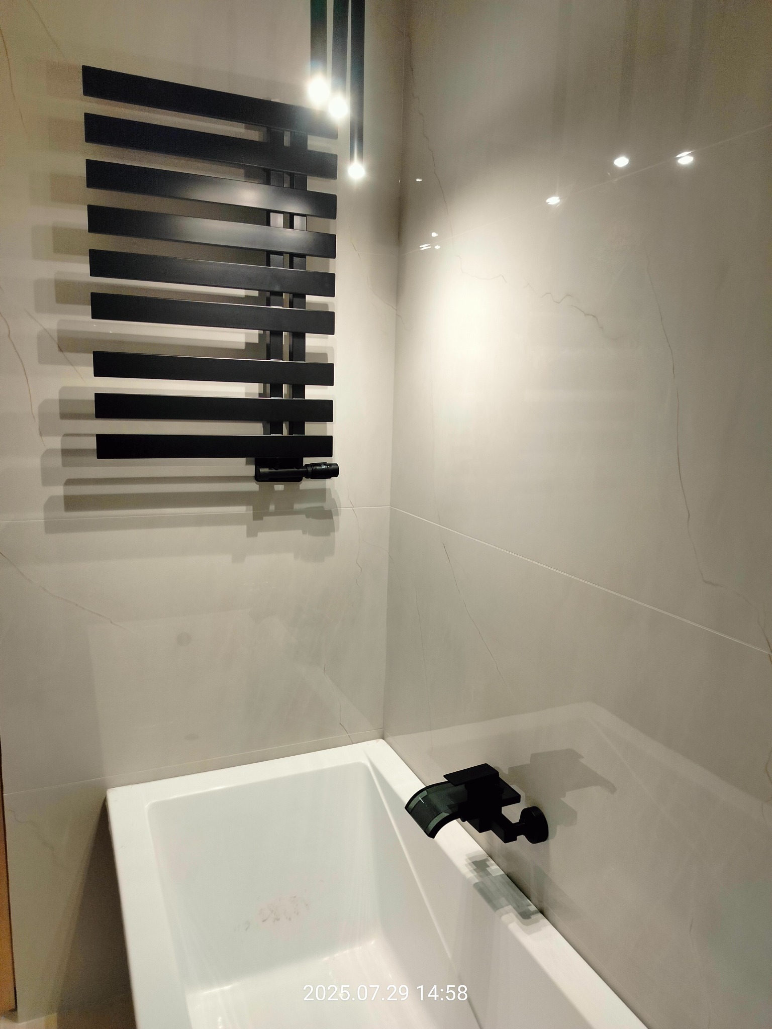 Wykończona łazienka w Kwidzynie: biała wanna z czarną armaturą, grzejnik drabinkowy i marmurowe płytki ścienne. Nowoczesny design.