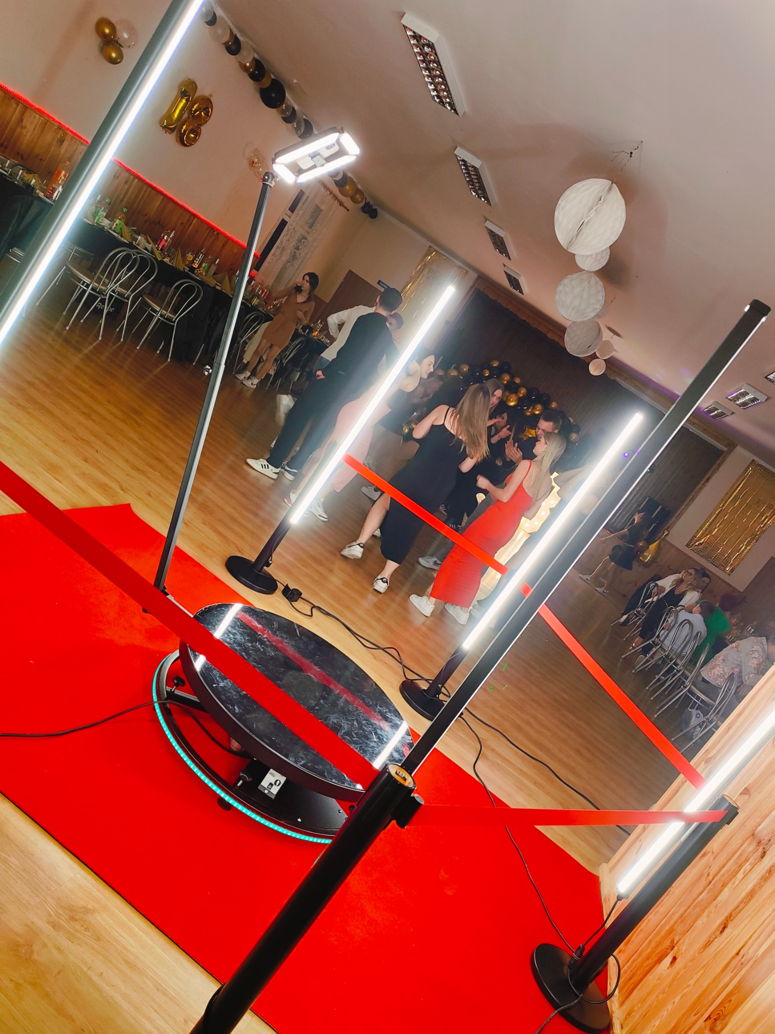 Automatyczna platforma obrotowa z oświetleniem LED na czerwonym dywanie, otoczona barierkami, w tle tańczący tłum na imprezie.