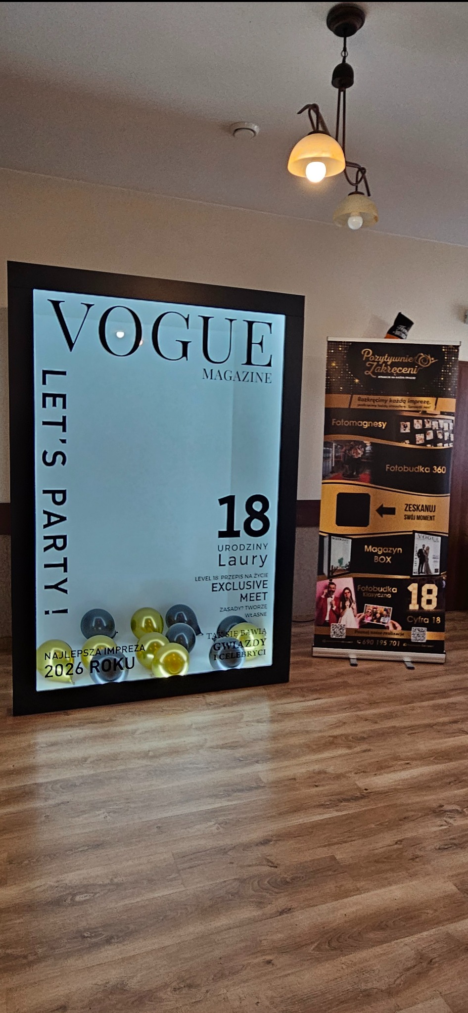 Atrakcja na 18 urodziny: podświetlana ścianka w stylu Vogue z balonami i baner reklamowy z ofertą fotobudki. Dekoracja imprezowa wewnątrz pomieszczenia.
