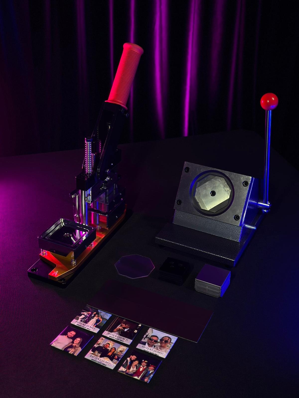 Prasa do magnesów z gotowymi, kwadratowymi magnesami ze zdjęciami, akrylowymi osłonkami i metalowymi elementami na czarnym tle, oświetlona fioletowo-różowym światłem.
