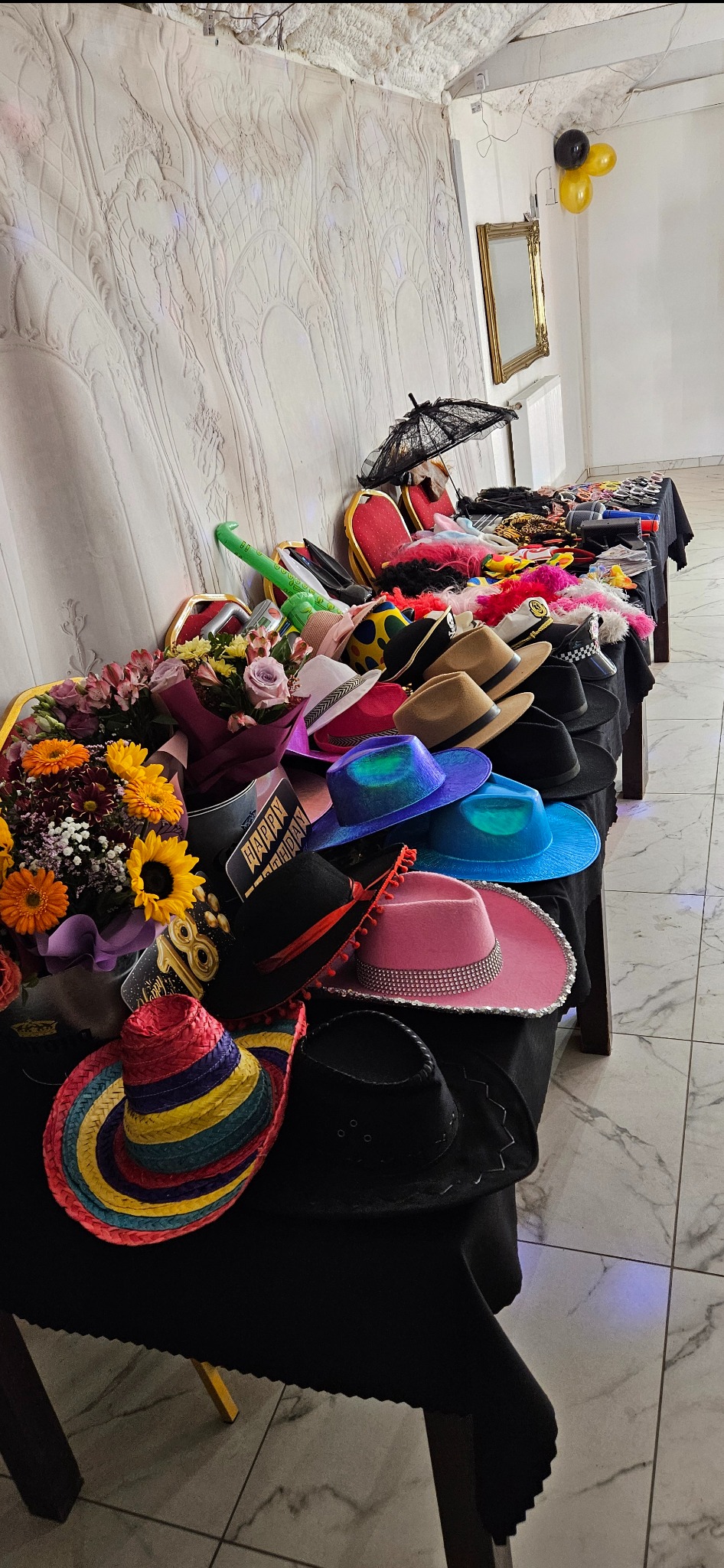 Stół z rekwizytami do sesji zdjęciowej: kapelusze, kwiaty, okulary, parasolka. Dekoracje urodzinowe w tle. Przygotowania do zabawy.