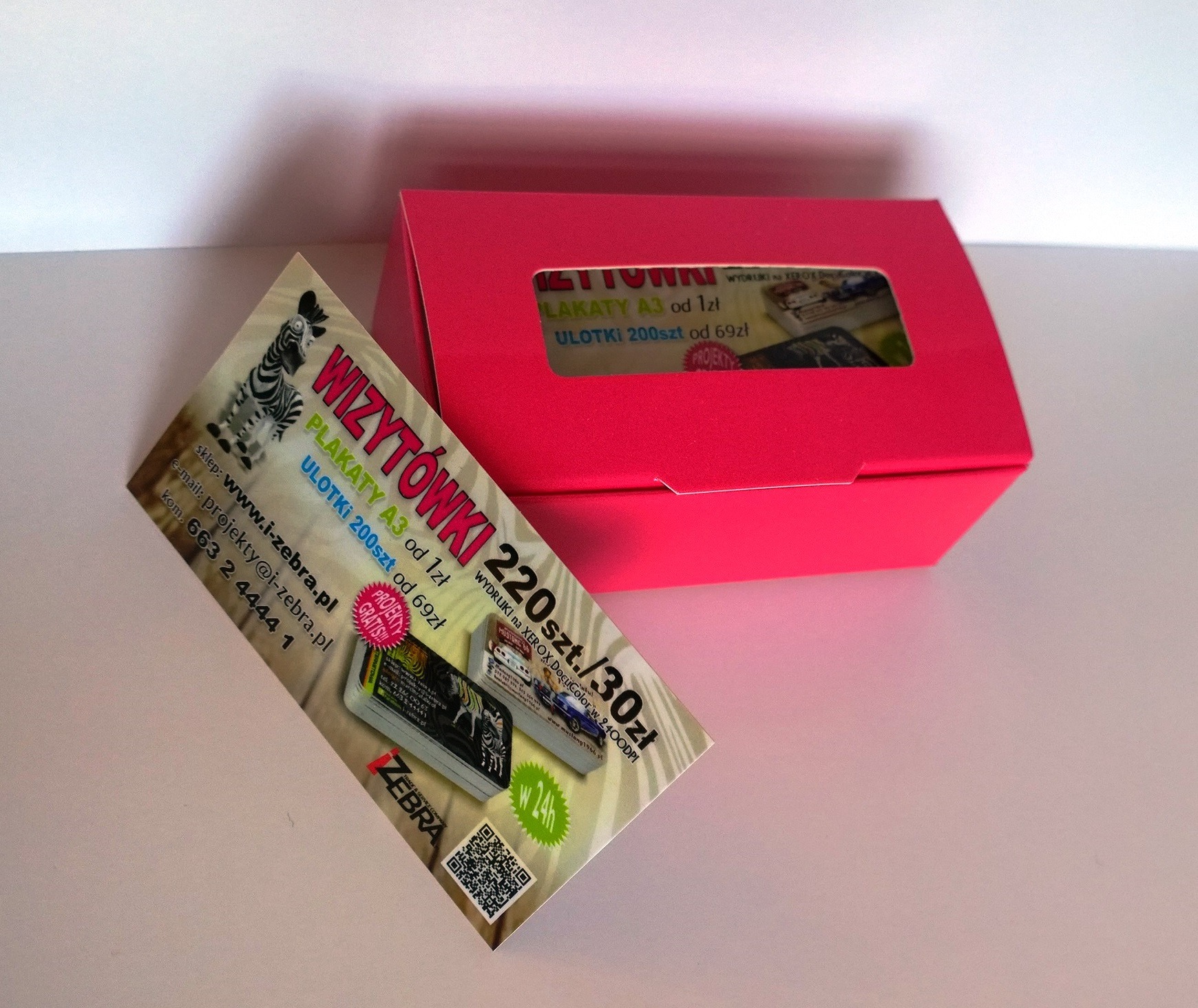 Różowa prezentacyjna skrzyneczka z okienkiem, obok niej próbka z cenami druku: 220 sztuk za 30 zł, z grafiką zebry i kodem QR.