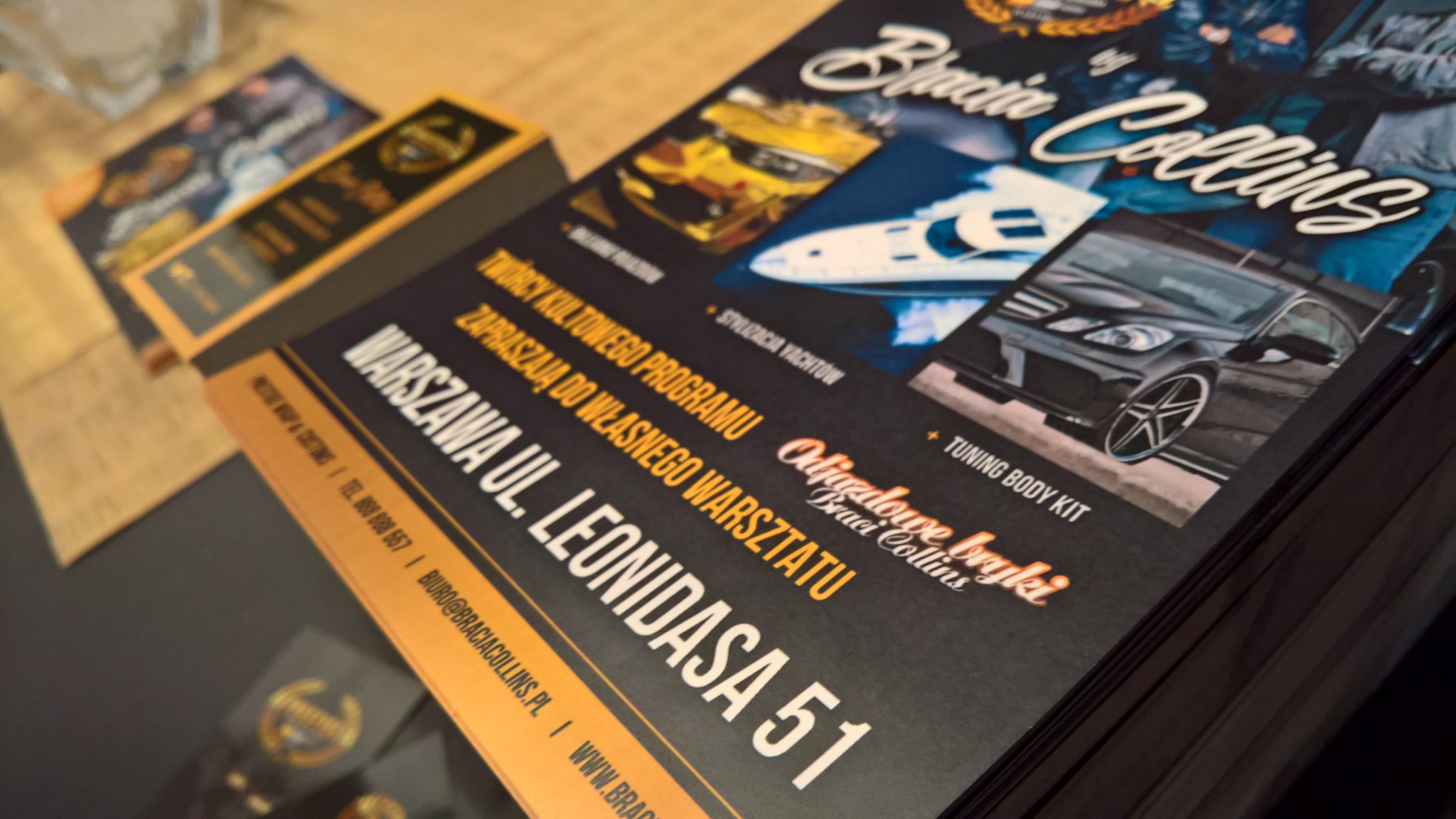 Stos ulotek i wizytówek z motywem tuningu samochodów i stylizacji jachtów, z adresem warsztatu w Warszawie.