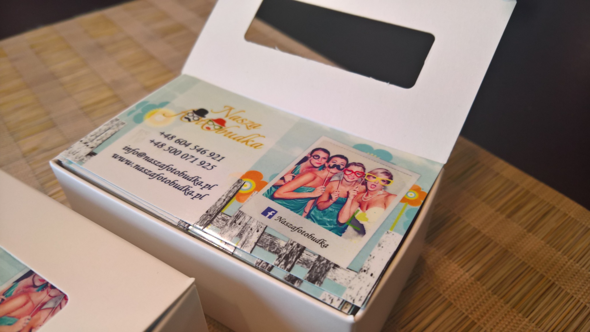 Pudełko z wizytówkami firmy NaszaFotobudka, z wizerunkiem trzech kobiet w przebraniach na polaroidowym zdjęciu.