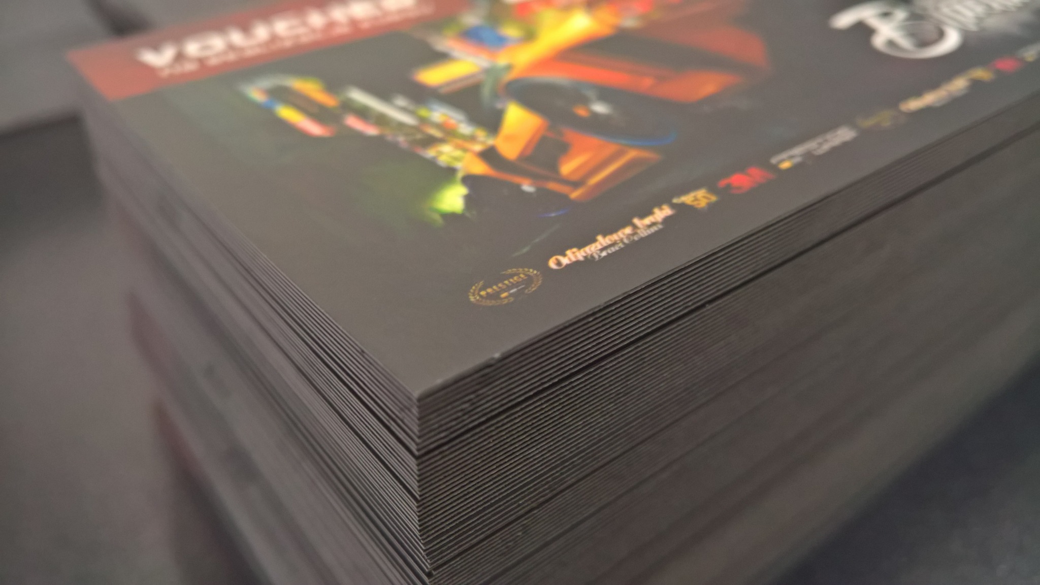 Stos czarnych, matowych voucherów z kolorową grafiką samochodu i złotymi logotypami firm partnerskich.