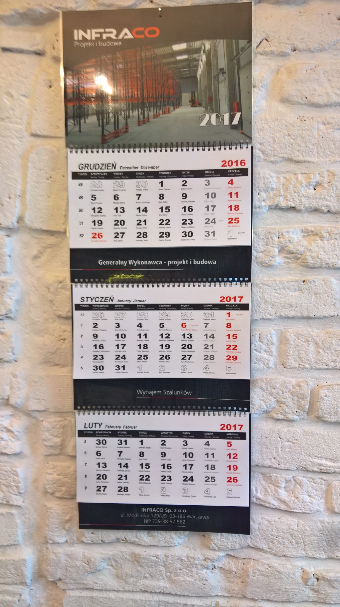 Kalendarz firmowy INFRACO na rok 2017 z widocznymi miesiącami grudzień 2016, styczeń i luty 2017, zawieszony na białej ceglanej ścianie.