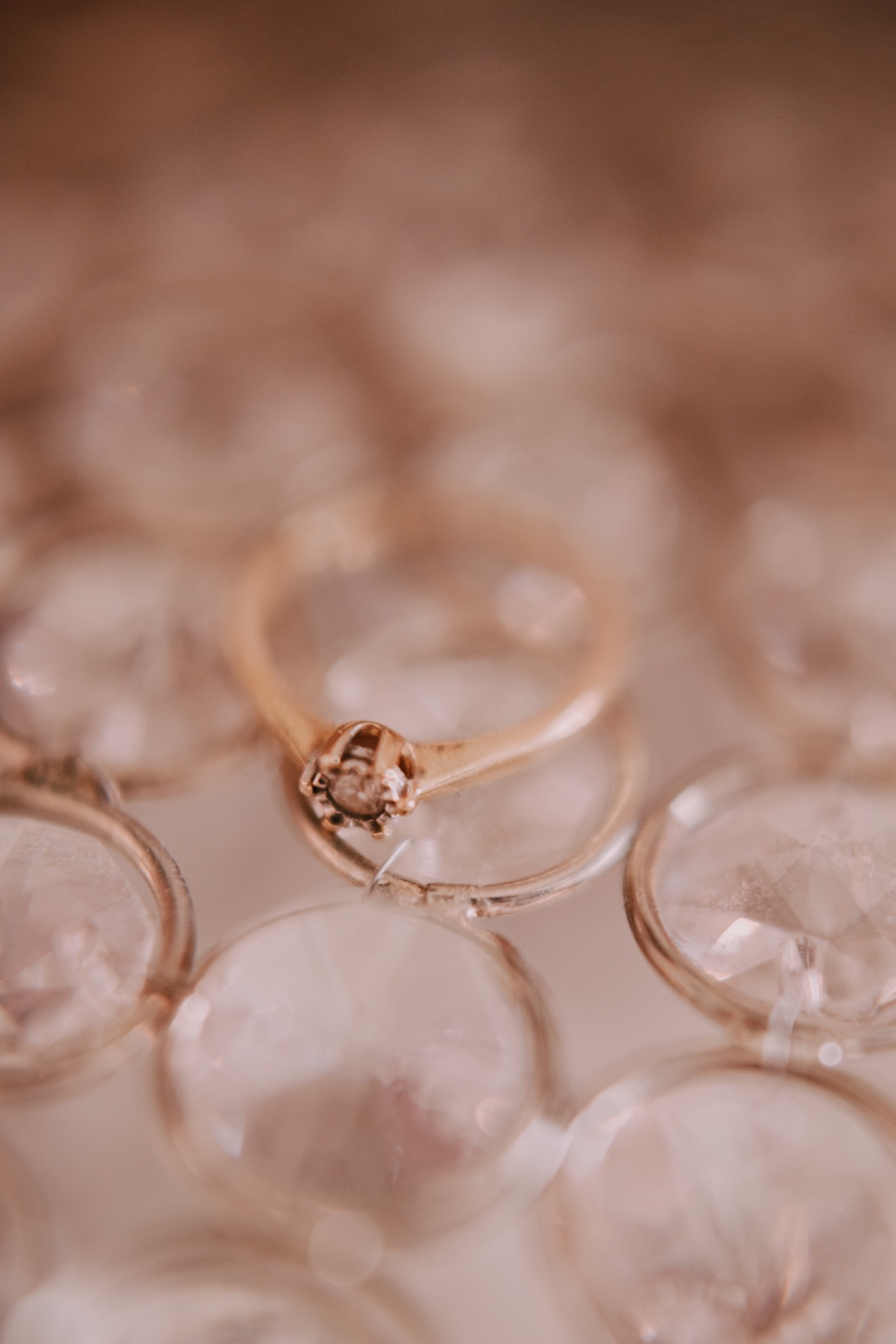 Złoty pierścionek zaręczynowy z diamentem, ułożony na szklanej powierzchni z fasetowanymi elementami, tworzącymi rozproszone światło i delikatne refleksy.